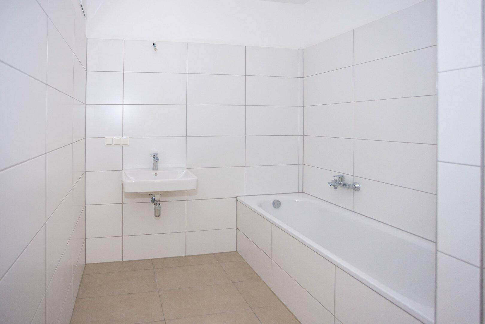 Helles Badezimmer mit Badewanne, Waschbecken und weißen Fliesen, bietet eine saubere Ästhetik.