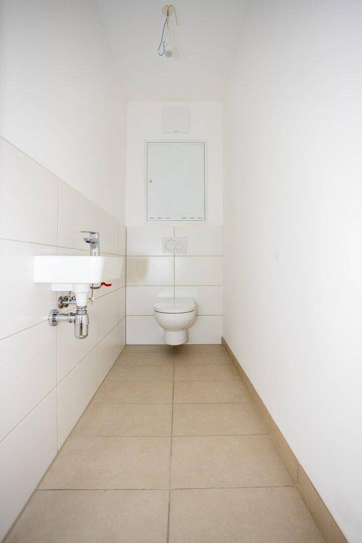 Kompaktes Gäste-WC mit Wand-WC, kleinem Waschbecken und hellen Fliesen, funktional und sauber.