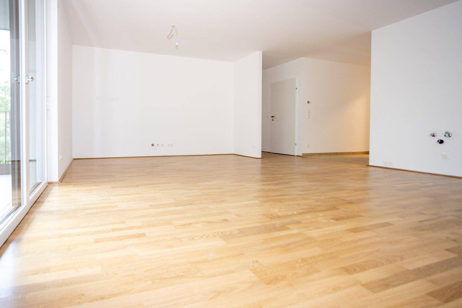 Geräumiges Wohnzimmer mit hellem Parkettboden und weißen Wänden, ideal für offene Wohnkonzepte.