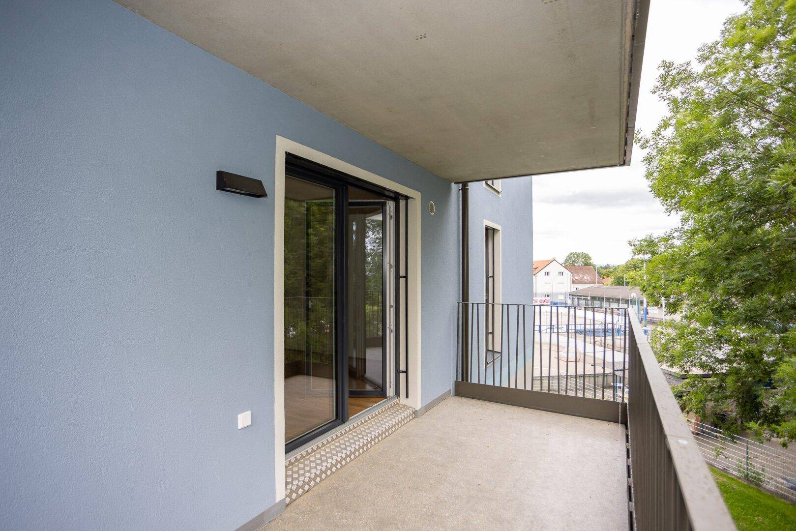 Moderner Balkon mit blauer Fassade und Blick auf die Umgebung, ideal für entspannte Stunden im Freien.