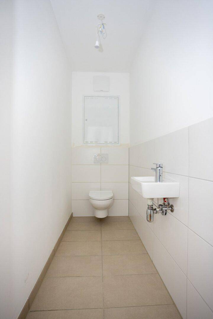 Separates Gäste-WC mit Wand-WC, kleinem Waschbecken und hellen Fliesen, praktisch und funktional.