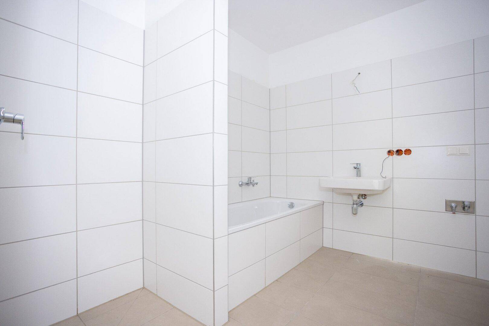Modernes Badezimmer mit weißen Fliesen, integrierter Badewanne und Waschbecken, noch ungenutzt.