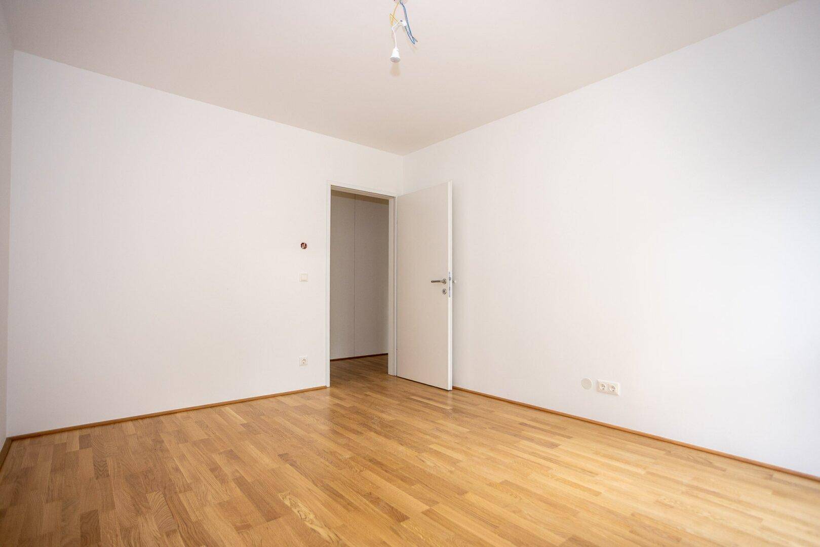Leeres Zimmer mit Parkettboden und weißen Wänden, bietet eine neutrale Basis für persönliche Gestaltung.
