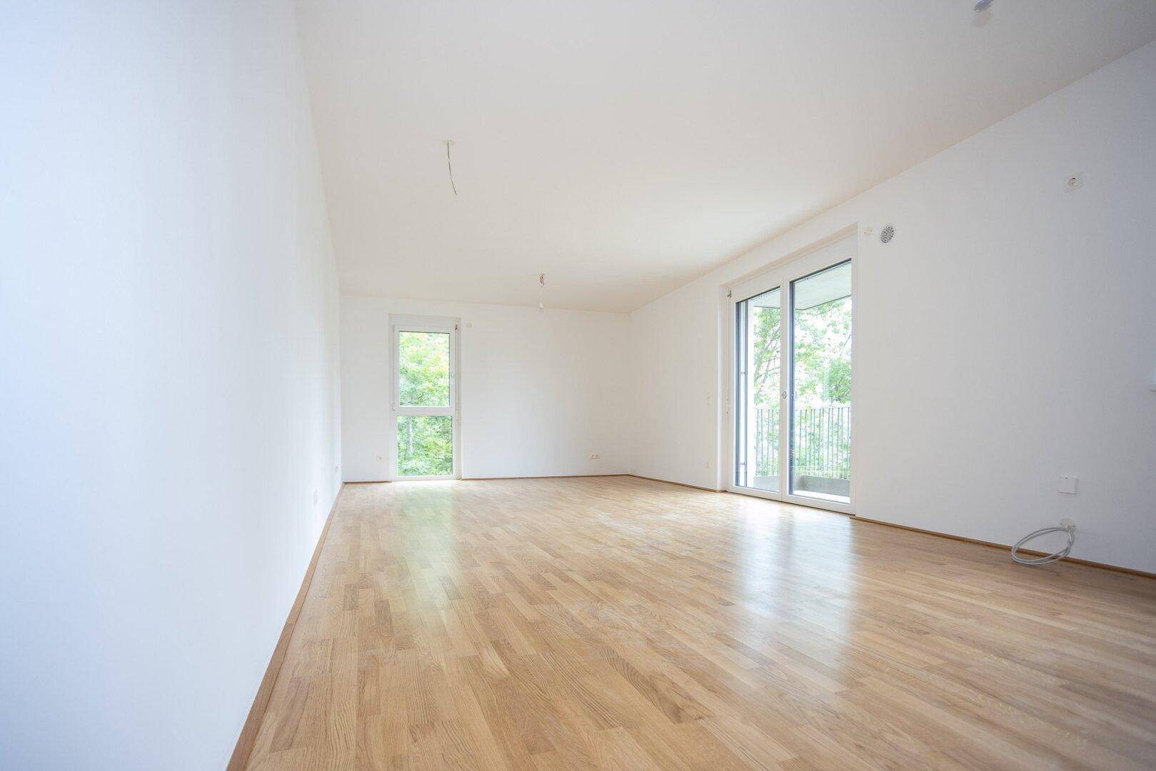 Helles, leeres Zimmer mit hellem Holzparkett und Zugang zu einem Balkon, ideal für Wohn- oder Schlafbereich.