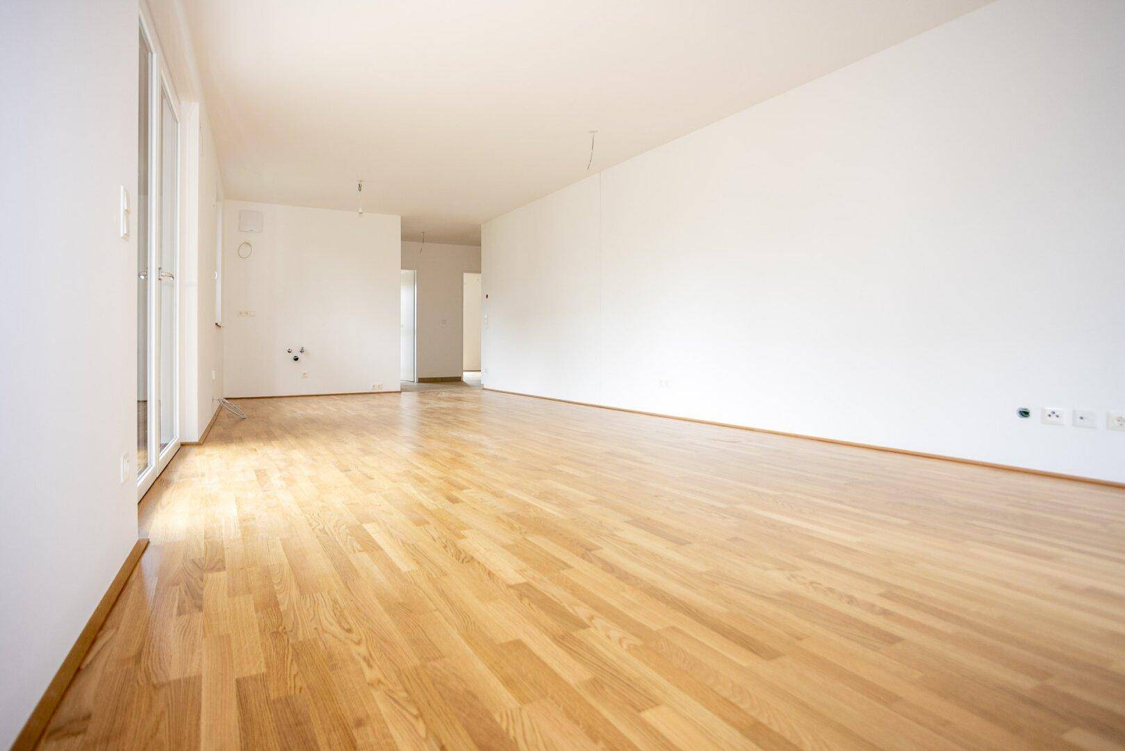 Heller, unmöblierter Raum mit glänzendem Holzparkett und großen Fenstern, bereit für individuelle Gestaltung.