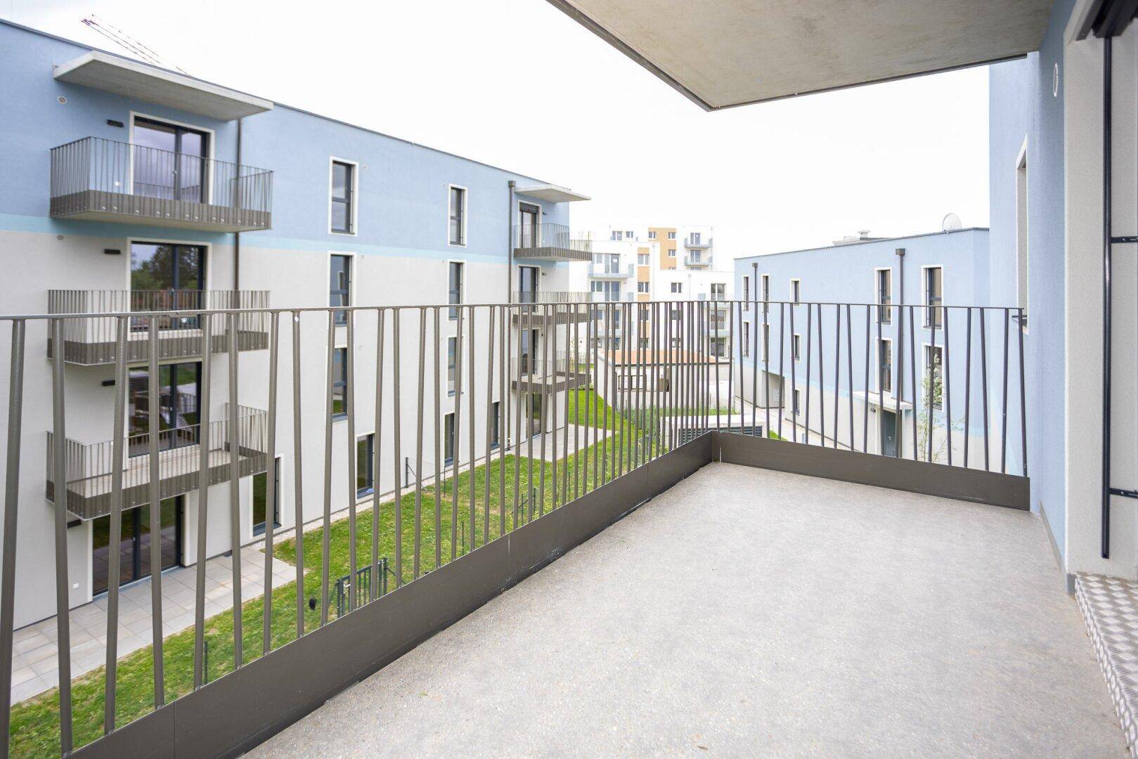 Geräumiger Balkon mit Metallgeländer und Blick auf die umliegenden Neubauten und den grünen Innenhof.