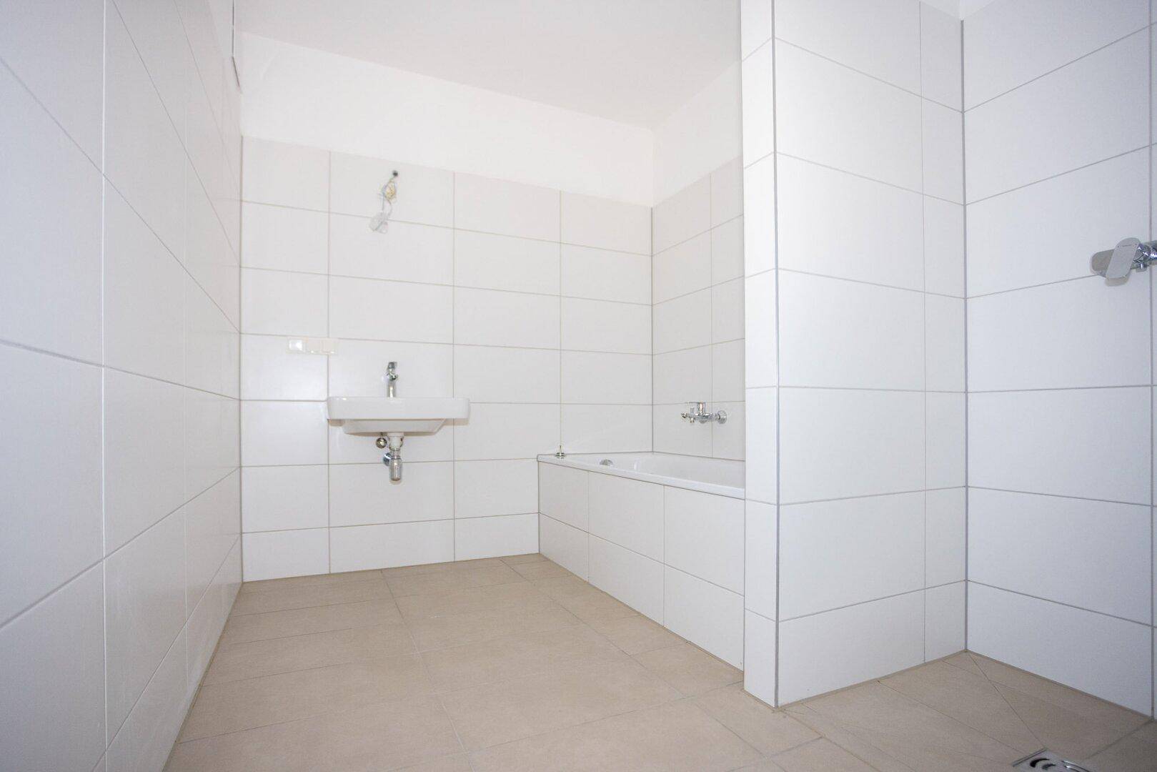 Modernes Badezimmer mit weißen Fliesen, beigem Boden und einer Badewanne sowie einem Waschbecken.