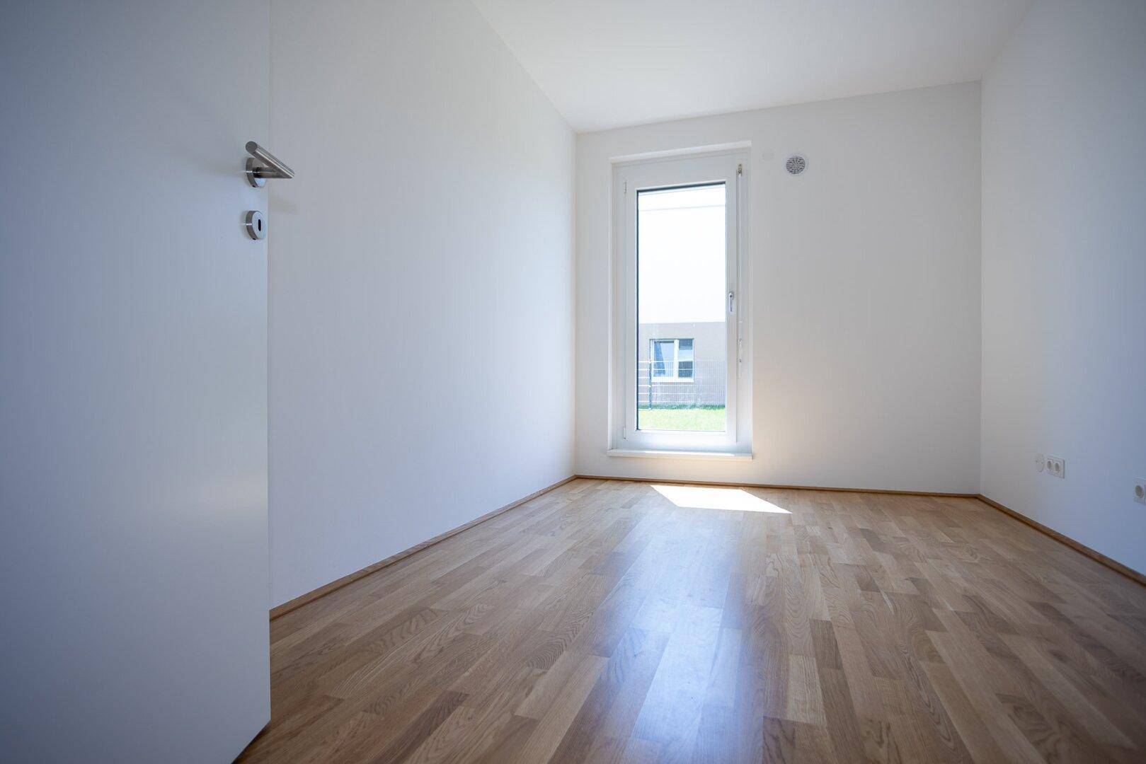 Helles Schlafzimmer mit Holzboden und einem großen Fenster, das viel Tageslicht hereinlässt.