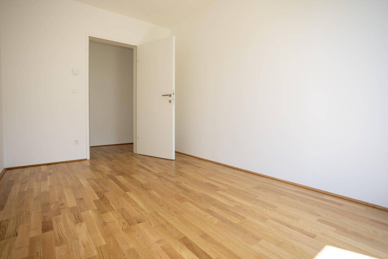 Leeres Zimmer mit Holzboden und weiß gestrichenen Wänden, ideal als Schlaf- oder Arbeitszimmer.