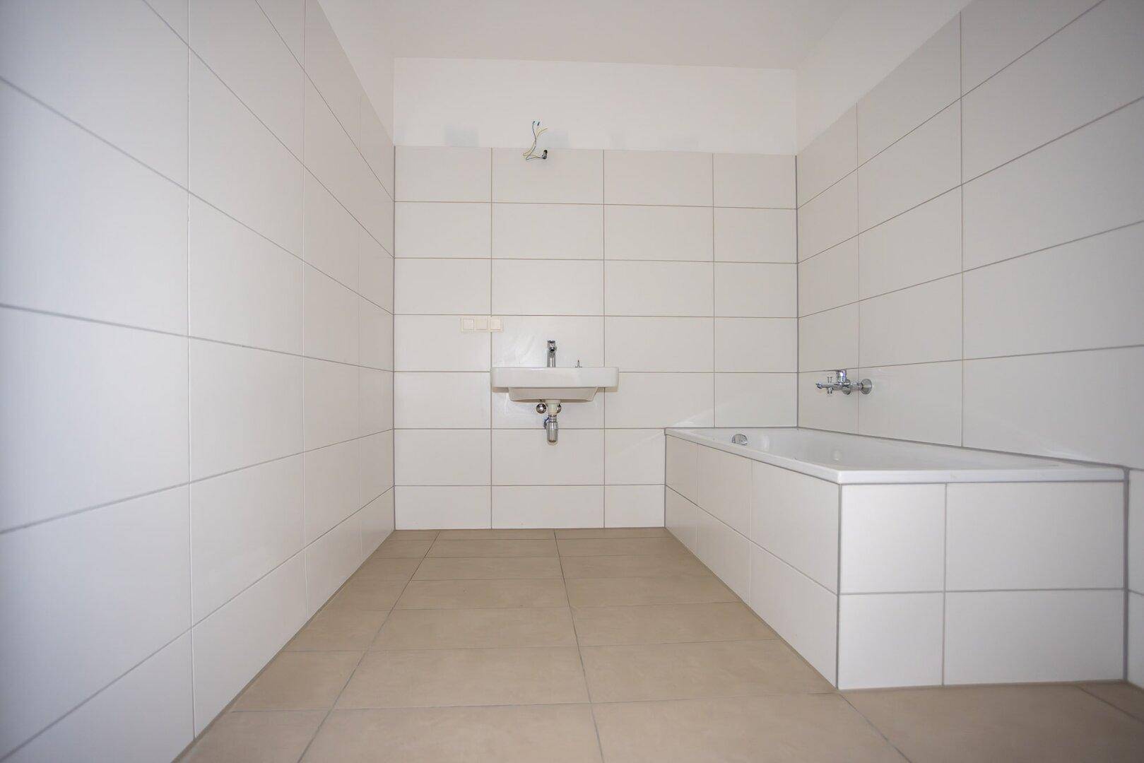 Unfertiges Badezimmer mit weißen Fliesen an den Wänden und beigen Bodenfliesen, bereit für die Installation.