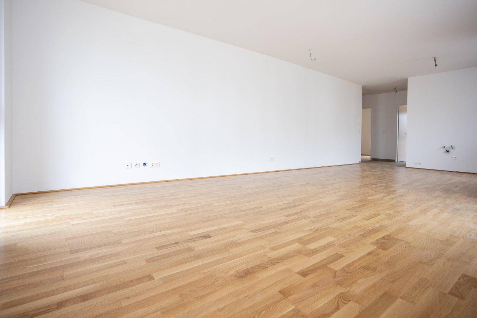Geräumiges, leeres Wohnzimmer mit hellem Parkettboden und weißen Wänden, bereit zum Einzug.