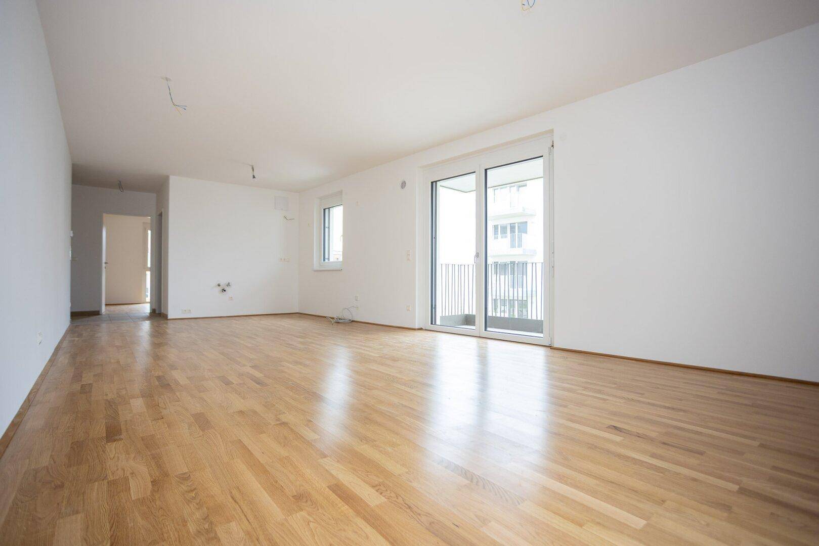Lichtdurchflutetes Wohnzimmer mit Parkettboden und Schiebetür zum Balkon in einem Neubau.