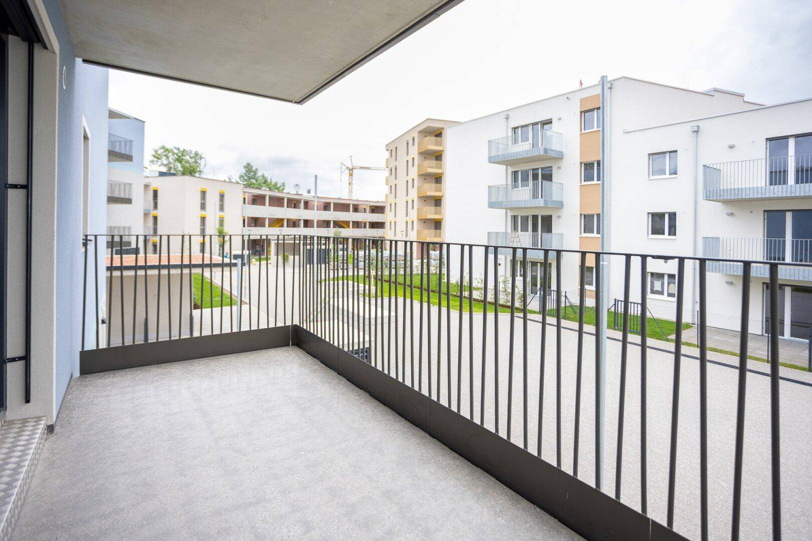 Moderner Balkon mit Blick auf die umliegenden Neubauten und Grünflächen der Wohnanlage.