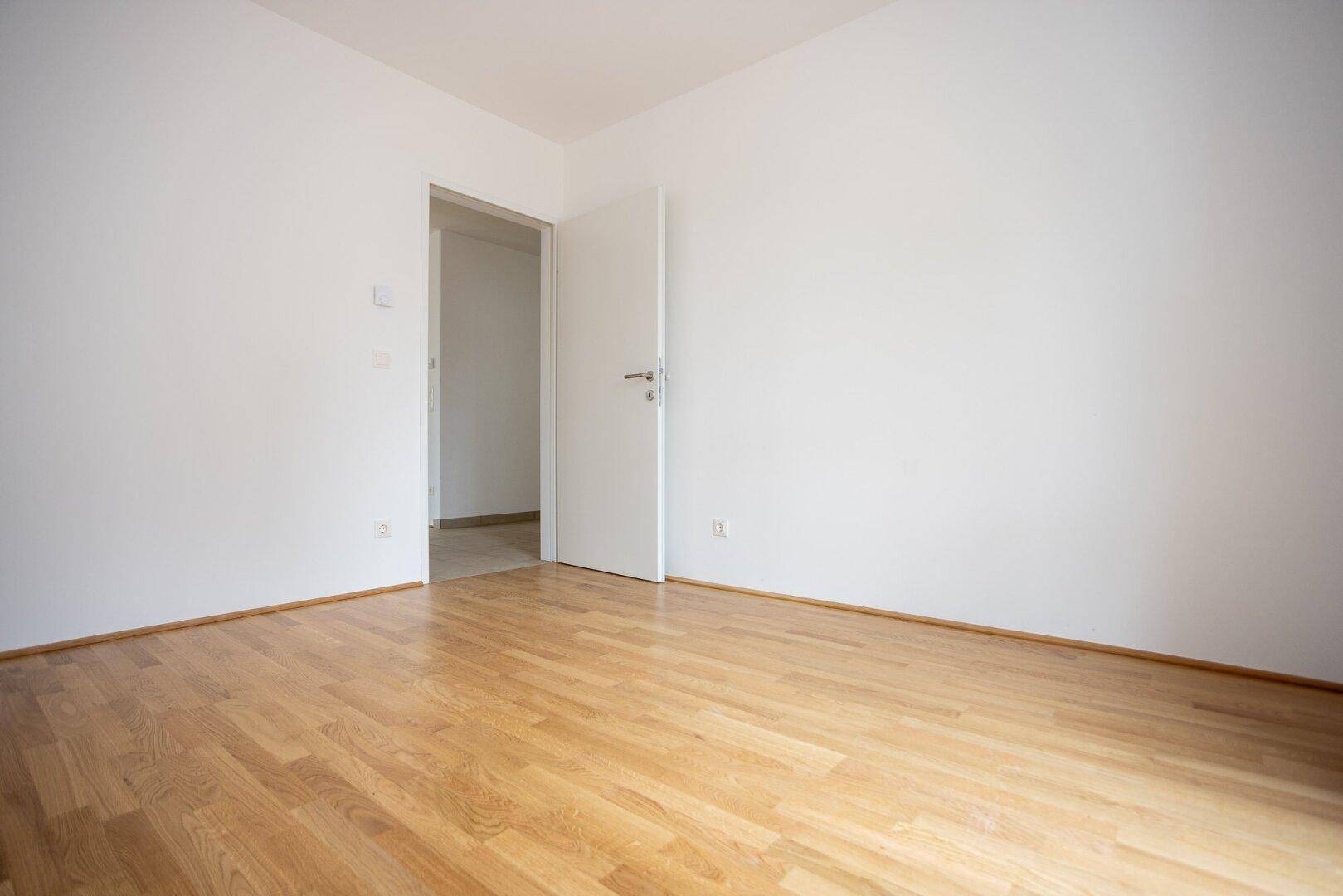 Leeres Schlafzimmer mit Parkettboden und weiß gestrichenen Wänden, bereit zur individuellen Gestaltung.