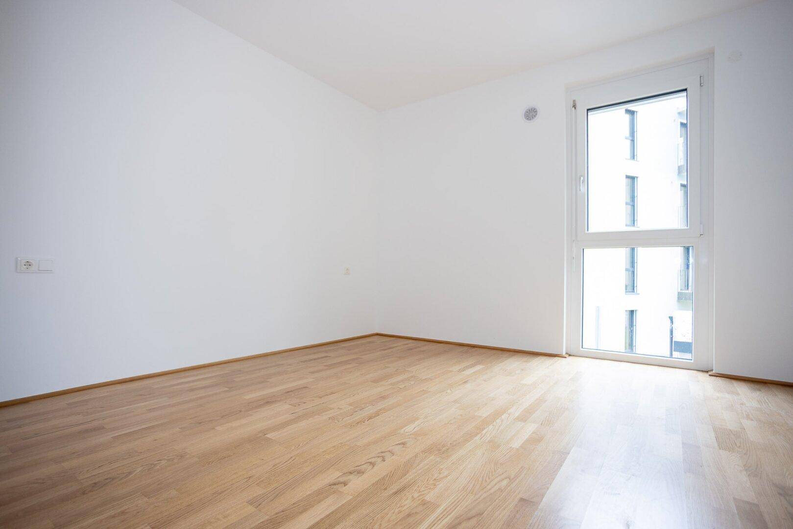 Freundliches Schlafzimmer mit Parkettboden und Fenster, das viel Tageslicht hereinlässt.