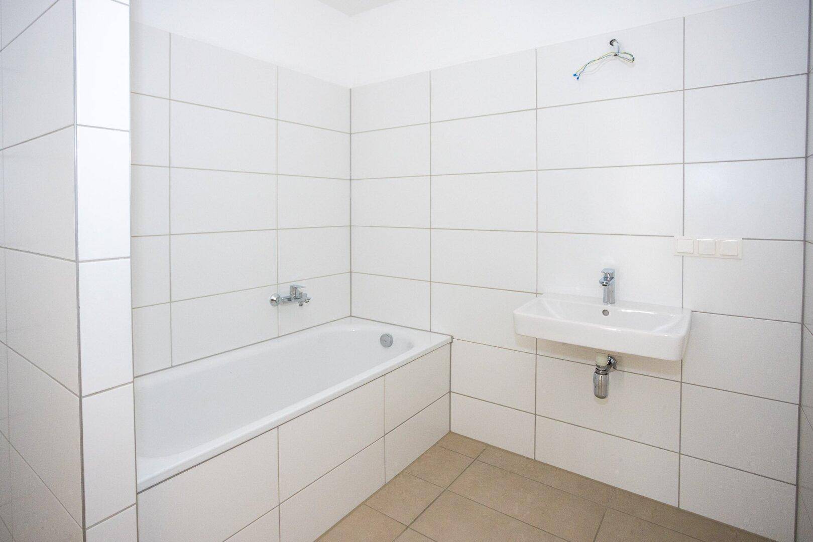 Helles Badezimmer mit Badewanne, Waschbecken und weißen Wandfliesen, sehr gepflegt.
