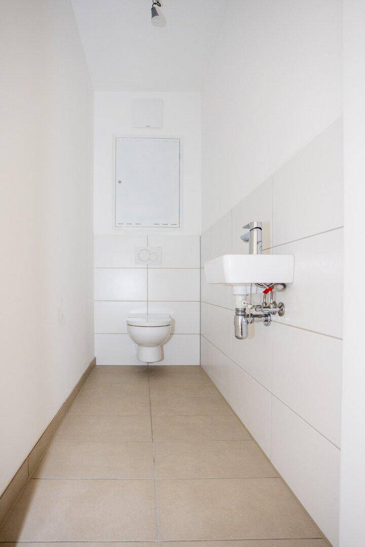 Separates Gäste-WC mit wandhängender Toilette und kleinem Waschbecken, modern gefliest.