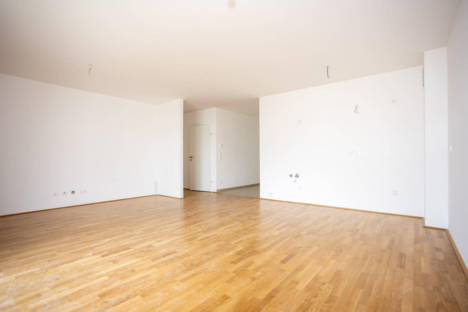 Geräumiges, leeres Zimmer mit Parkettboden und weiß gestrichenen Wänden, bereit zur individuellen Gestaltung.