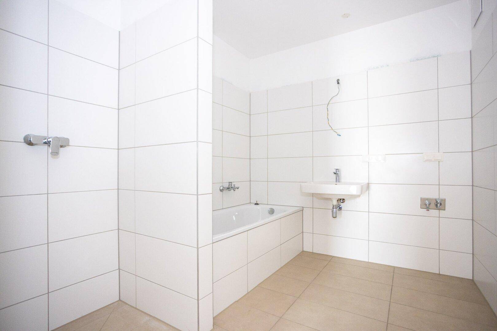 Modernes Badezimmer mit weißen Fliesen, Badewanne und Duschbereich, noch unfertig.