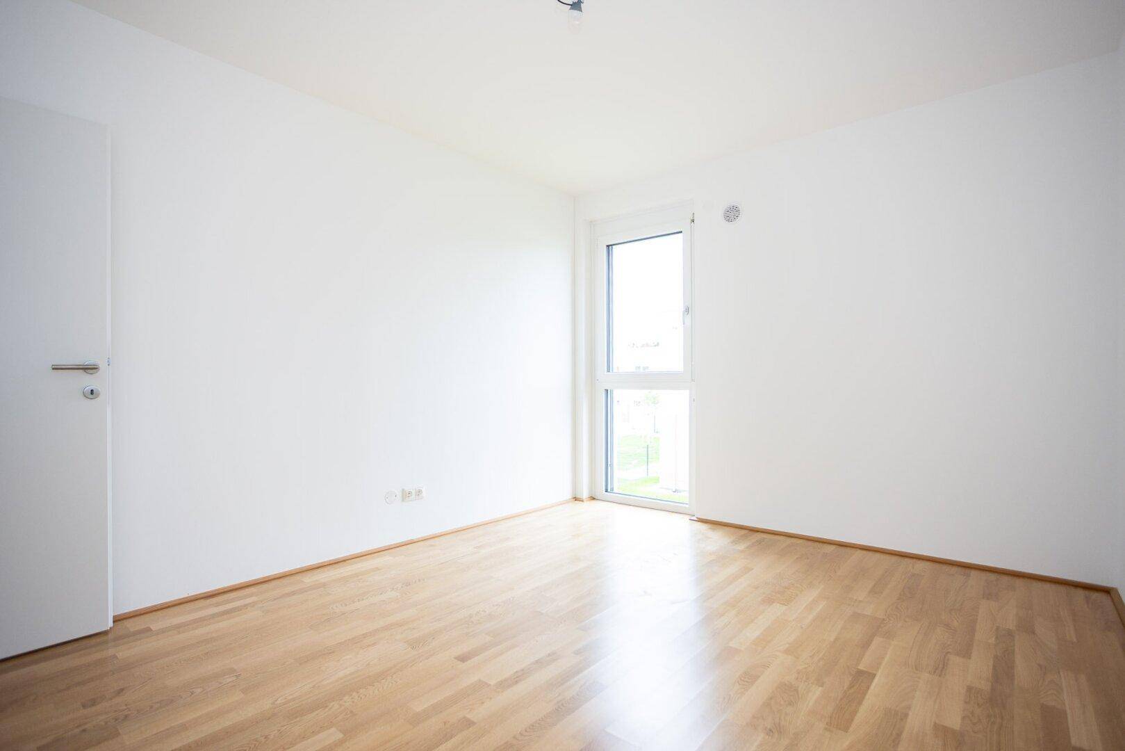 Leeres Schlafzimmer mit Parkettboden und weiß gestrichenen Wänden, bereit zum Einzug und zur Einrichtung.