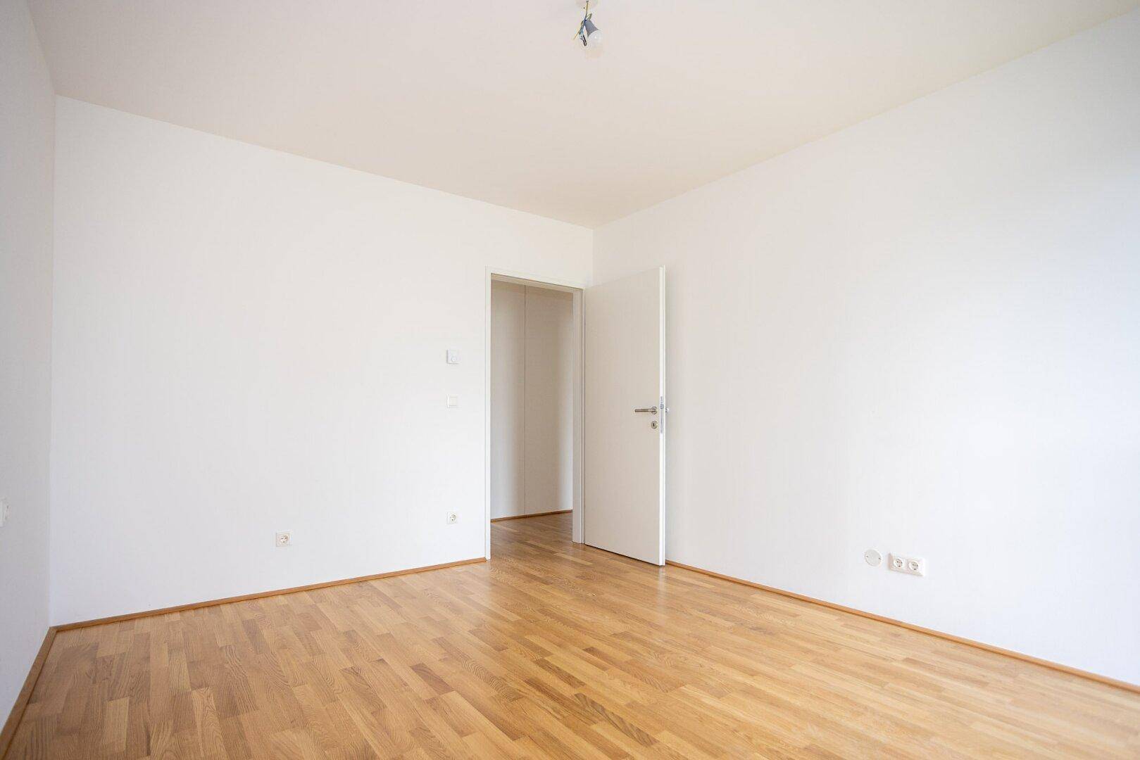 Helles Zimmer mit Parkettboden und offener Tür, ideal als Schlaf- oder Arbeitszimmer nutzbar.