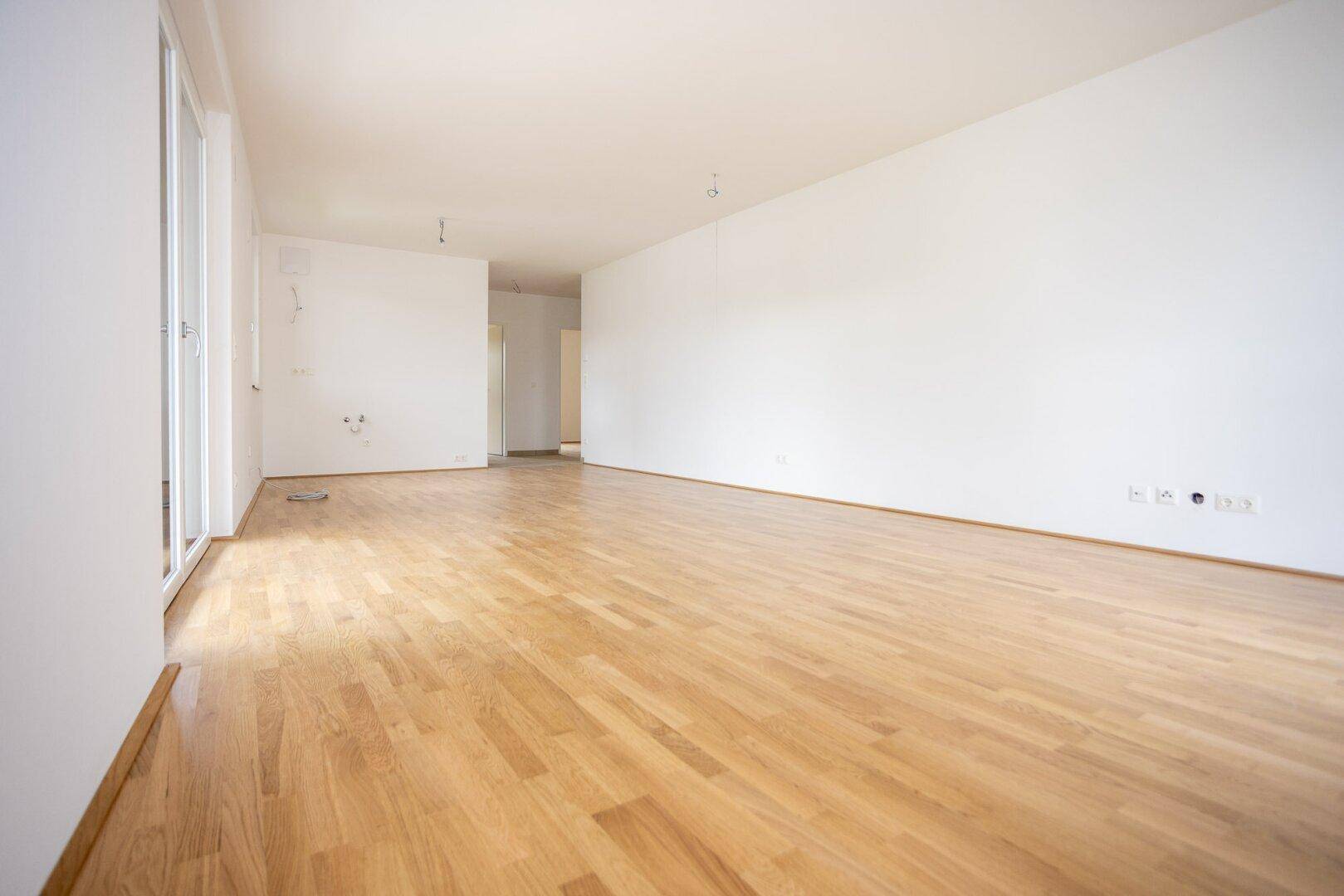 Weitläufiger, heller Raum mit Parkettboden und viel Tageslicht, ideal für Wohnbereiche.