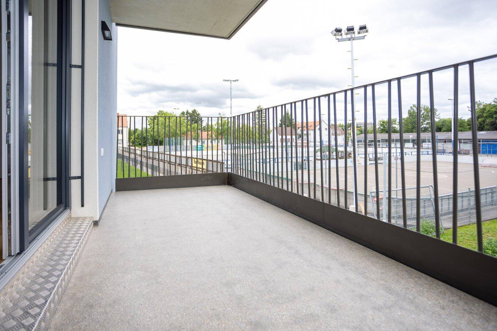 Balkon mit Ausblick auf Sportanlagen und die umliegende Nachbarschaft unter bewölktem Himmel.