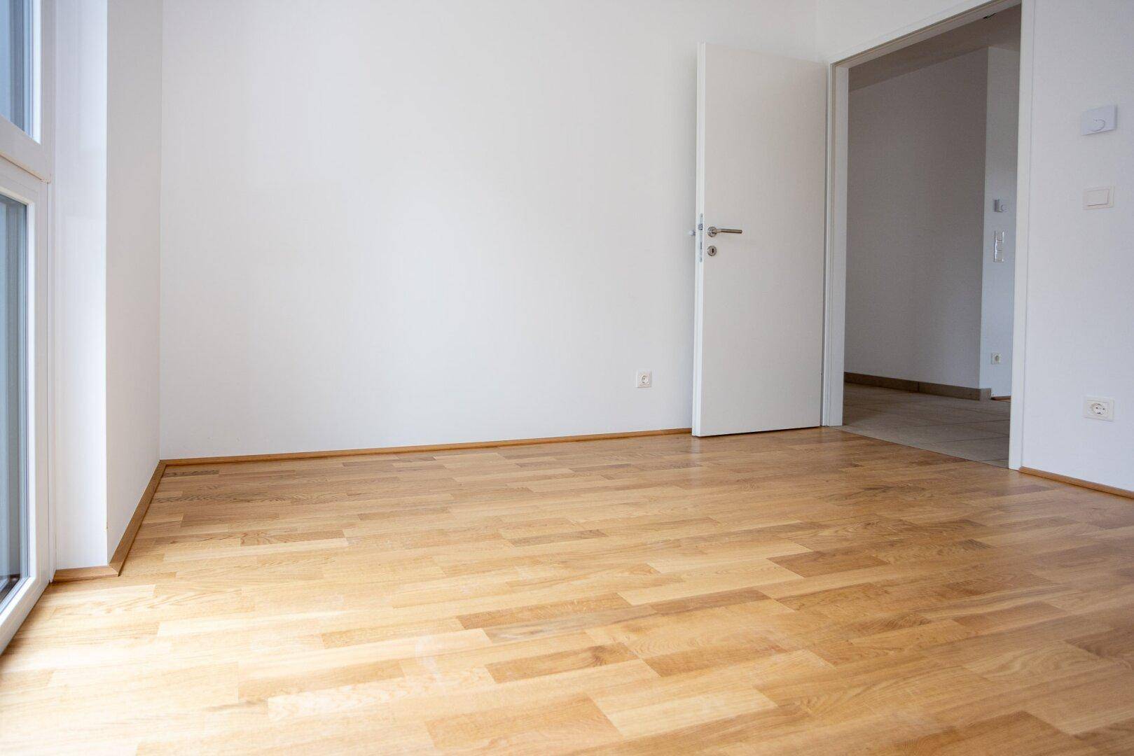Leeres Zimmer mit Parkettboden und Zugang zu einem weiteren Raum, ideal als Schlafzimmer.