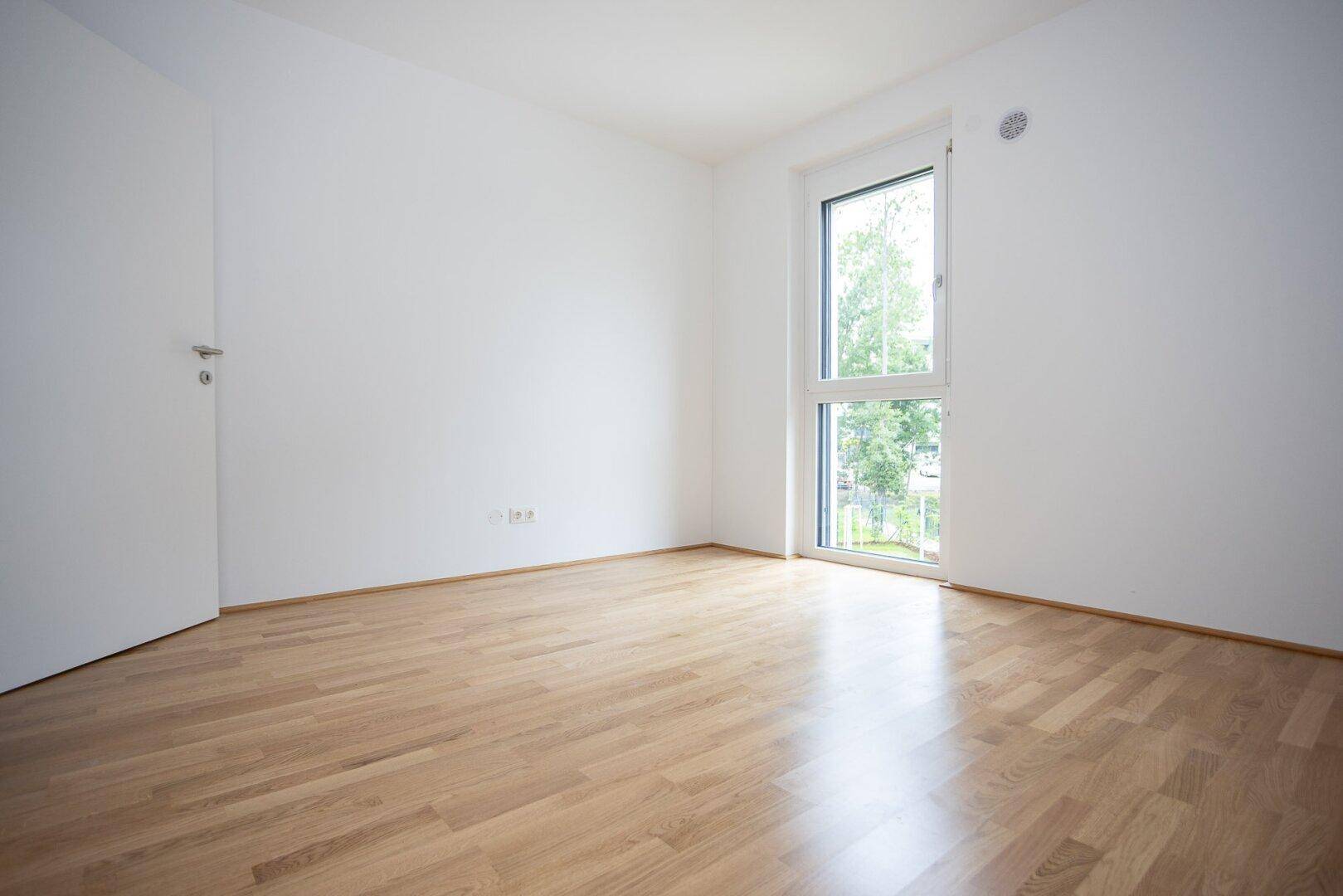 Helles Zimmer mit Parkettboden und großem Fenster, das eine angenehme Atmosphäre schafft.