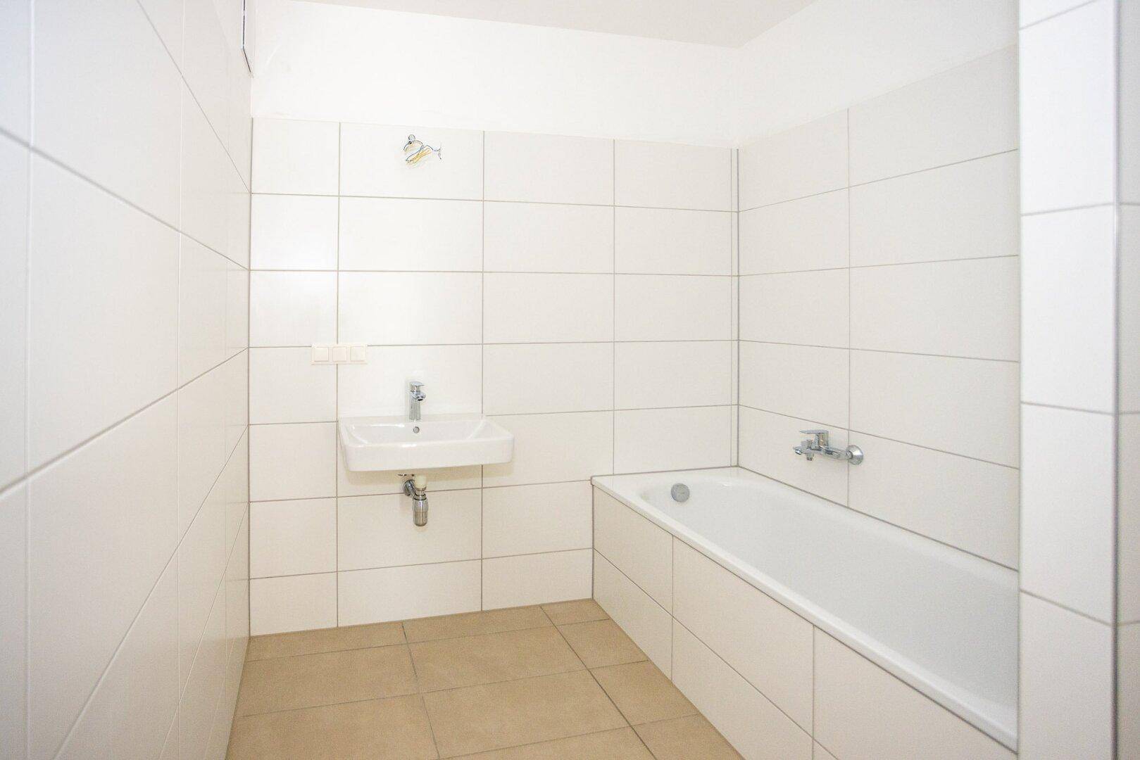 Helles Badezimmer mit Badewanne, Waschbecken und neutralen Bodenfliesen, sehr gepflegt.