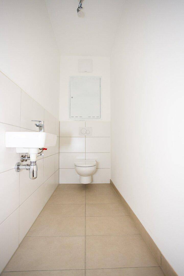 Separates Gäste-WC mit wandhängender Toilette und kleinem Waschbecken, modern gefliest.