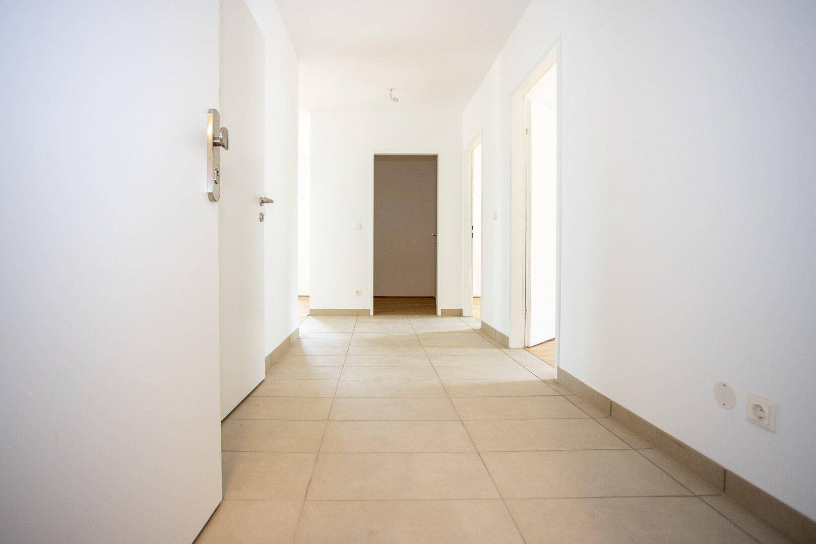 Heller Flur mit Fliesenboden, der zu verschiedenen Räumen der Wohnung führt.