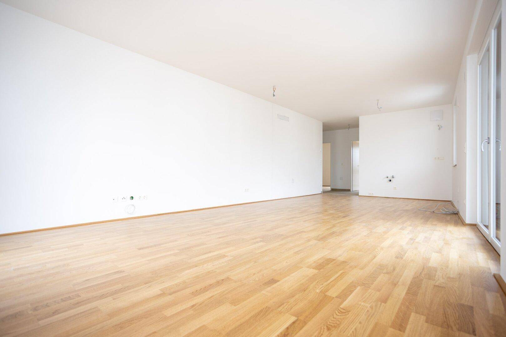 Geräumiges Wohnzimmer mit hellem Parkettboden und weißen Wänden, bereit zur Einrichtung.