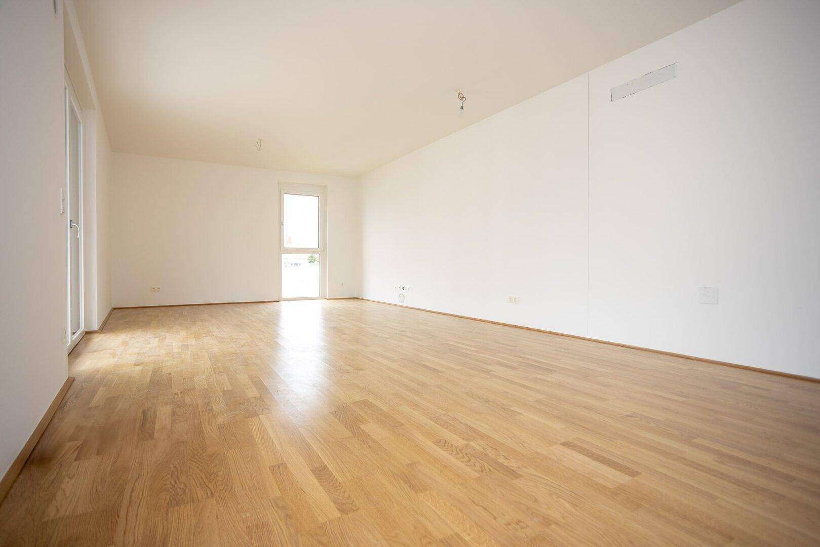 Lichtdurchfluteter Wohnbereich mit Holzboden und großen Fenstern, die viel Tageslicht hereinlassen.