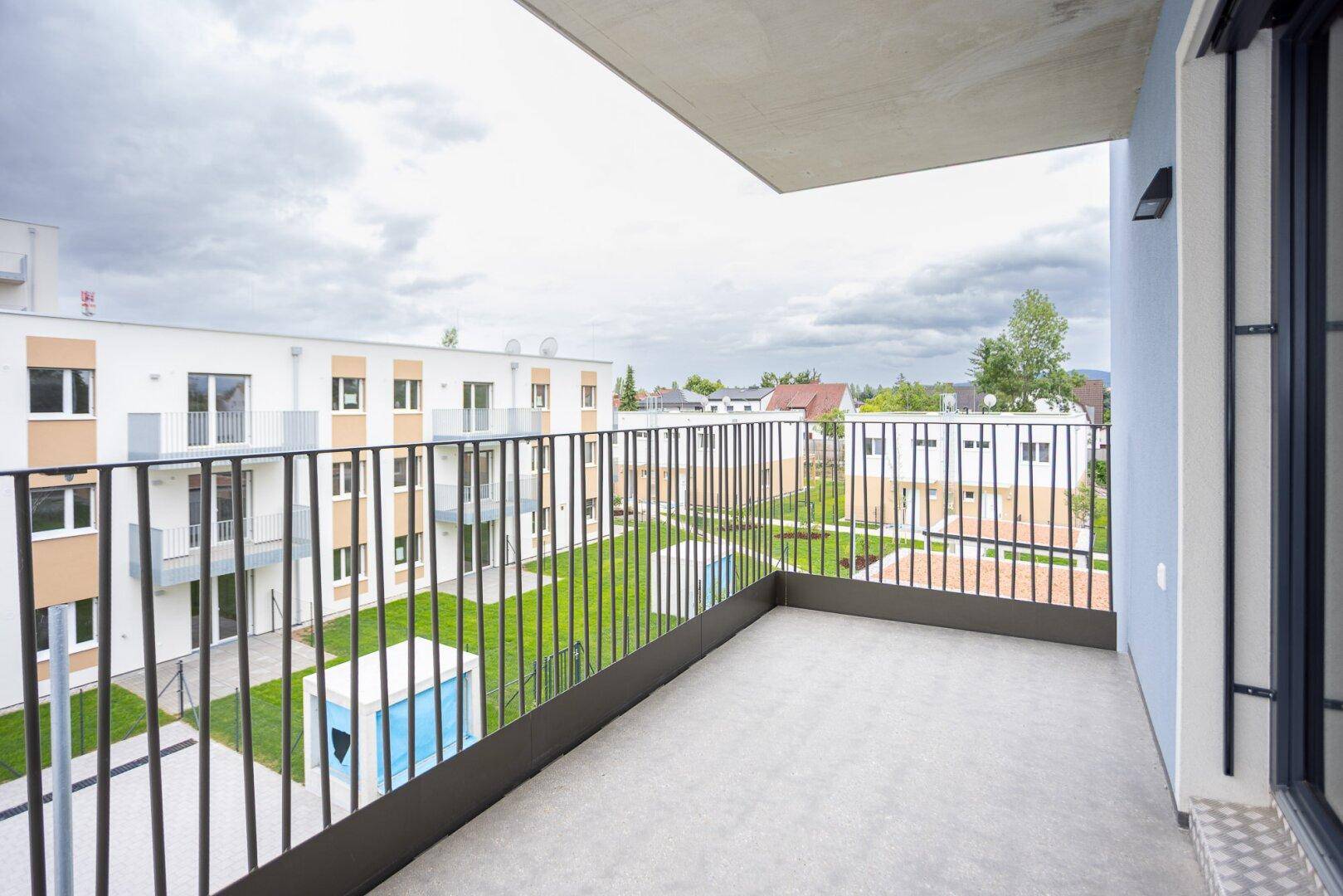 Geräumiger Balkon mit Metallgeländer und Blick auf die grüne Wohnanlage.