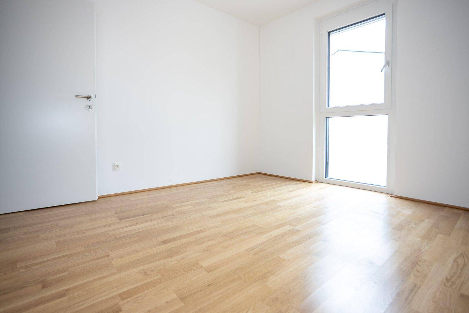 Leeres Schlafzimmer mit hellem Parkettboden und weiß gestrichenen Wänden, bereit zur Gestaltung.