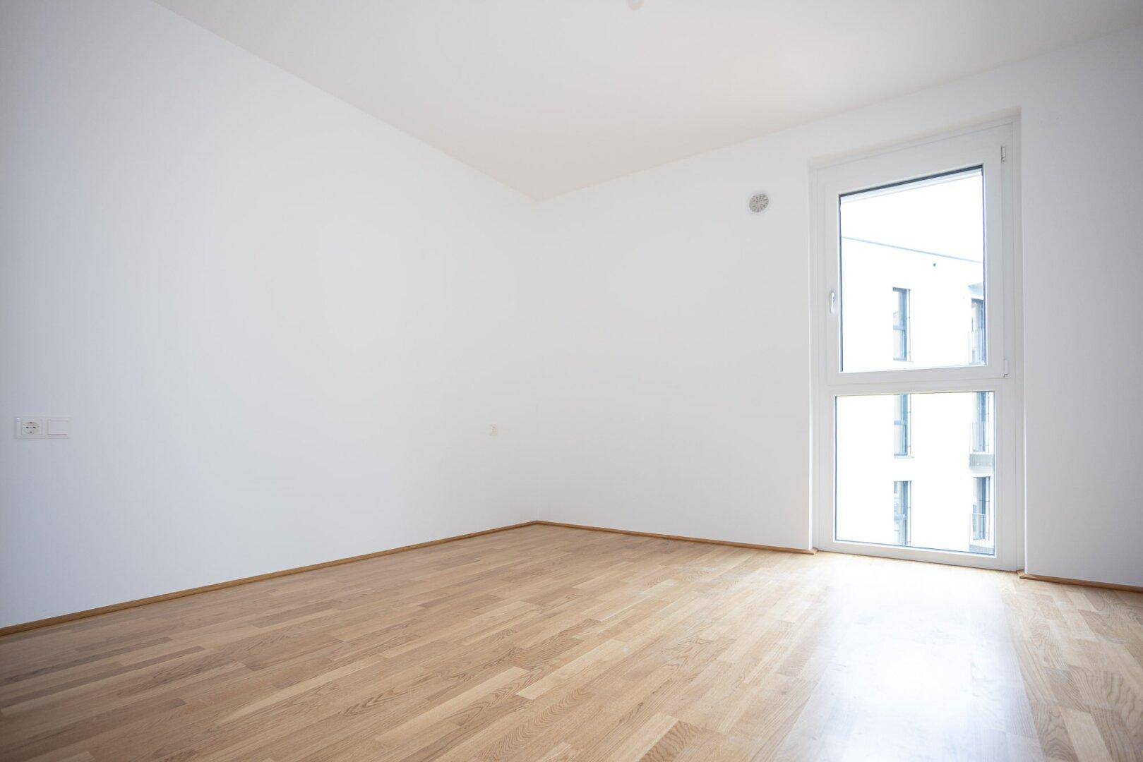 Modernes Schlafzimmer mit Holzboden und einem hohen Fenster, das den Raum erhellt.