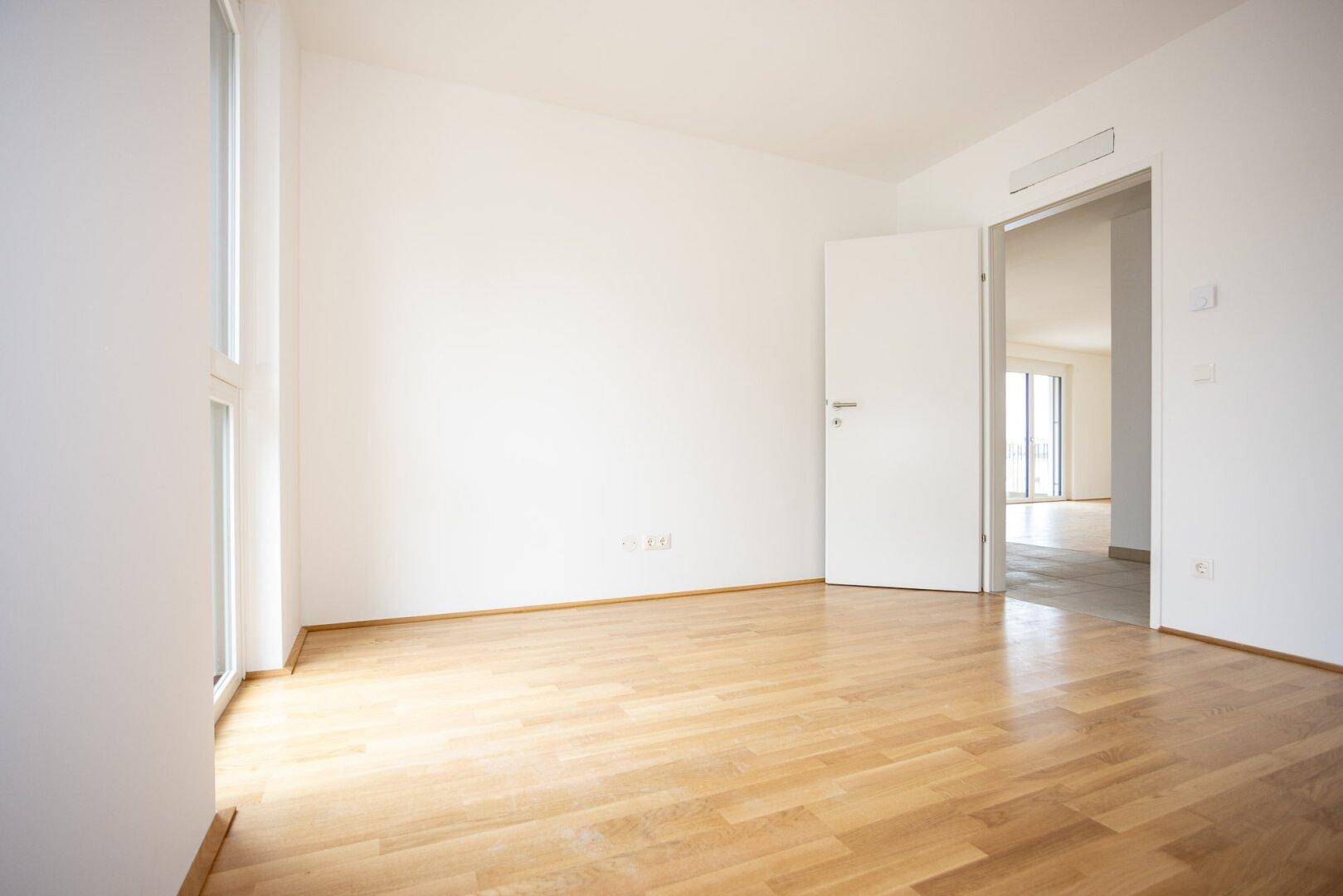 Helles Schlafzimmer mit Parkettboden und Zugang zu einem weiteren Raum, ideal für flexible Nutzung.