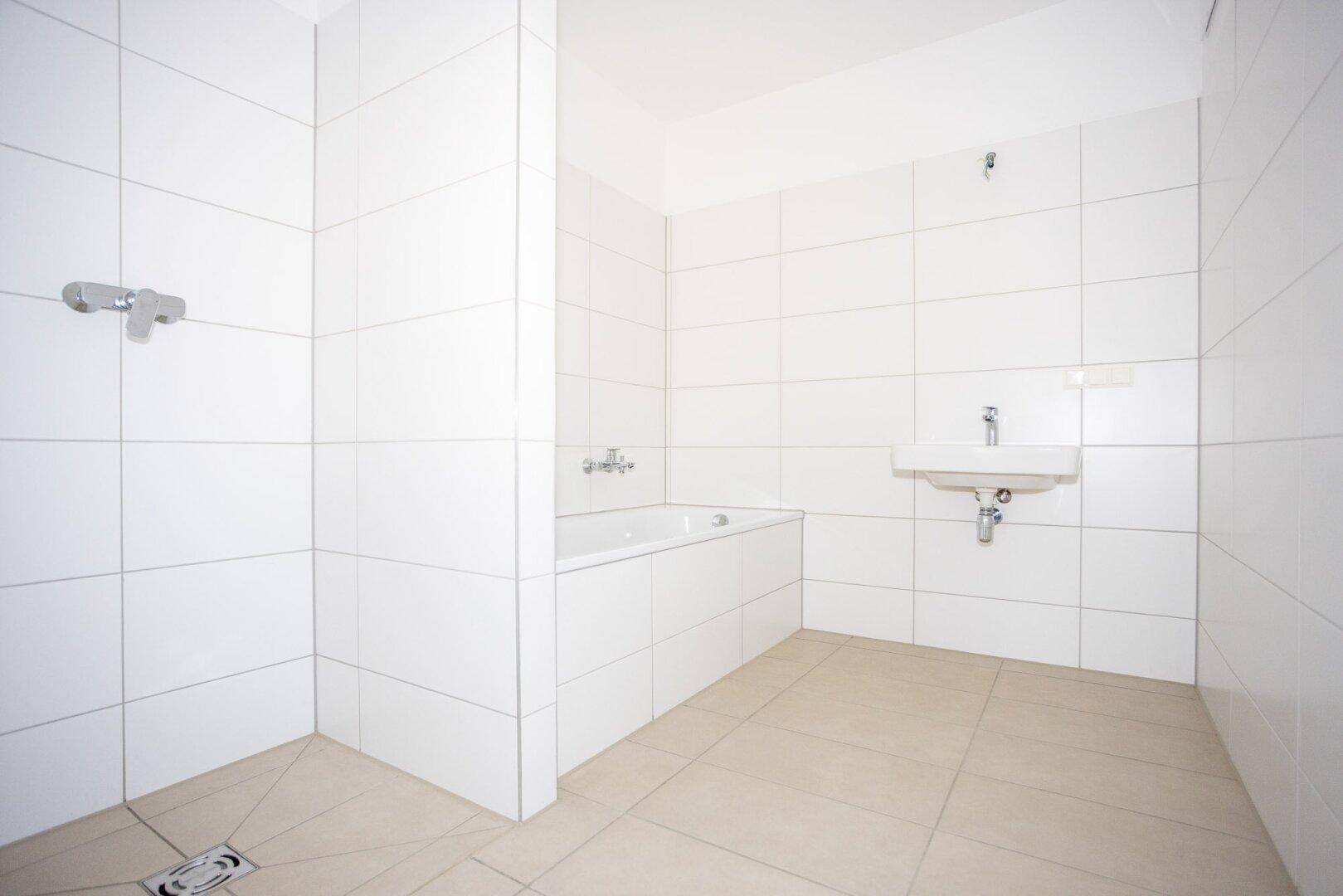 Modernes Badezimmer mit weißen Fliesen, Badewanne und Waschbecken, bereit zur Nutzung.