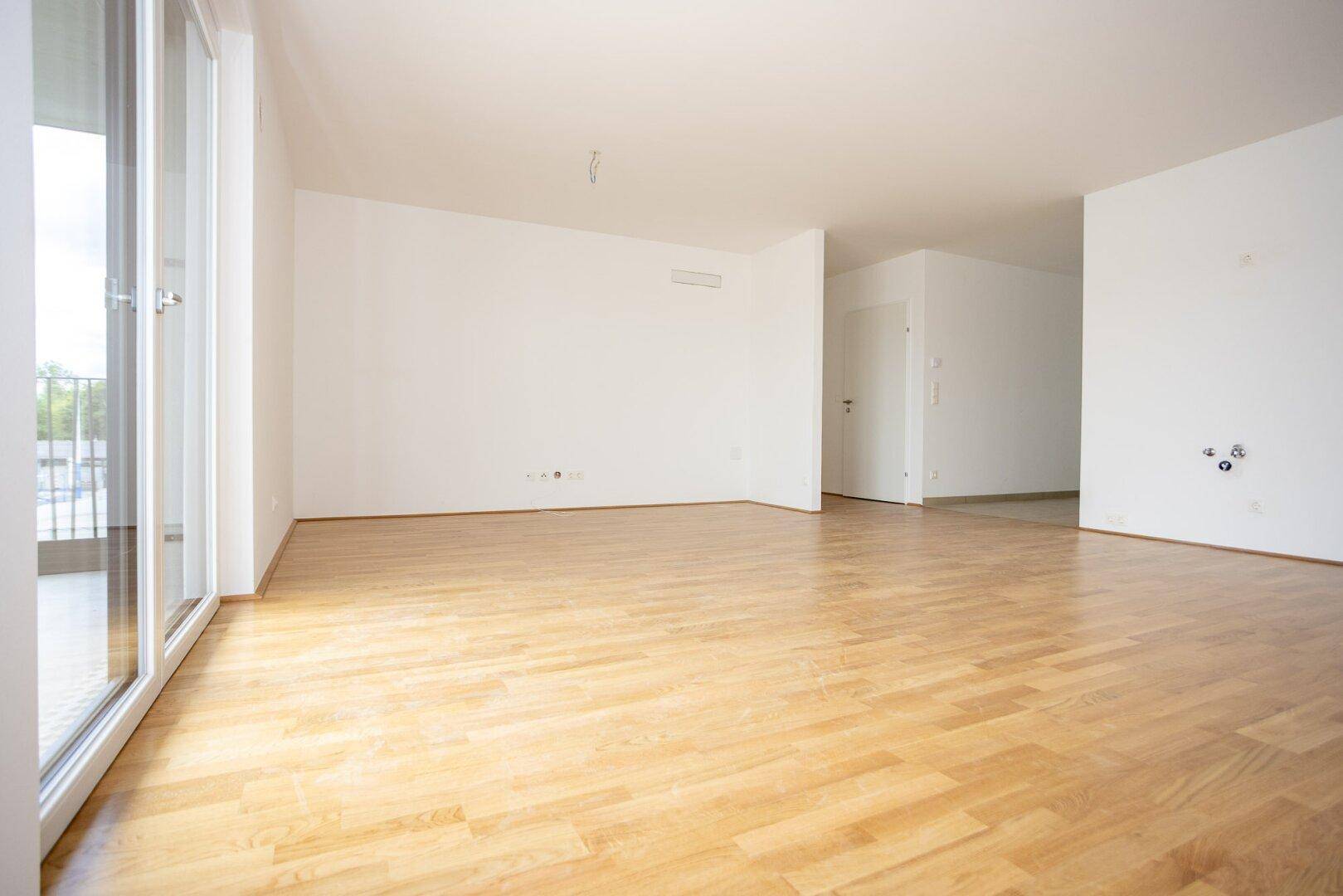 Geräumiges, helles Wohnzimmer mit Parkettboden und Blick auf den Flur.