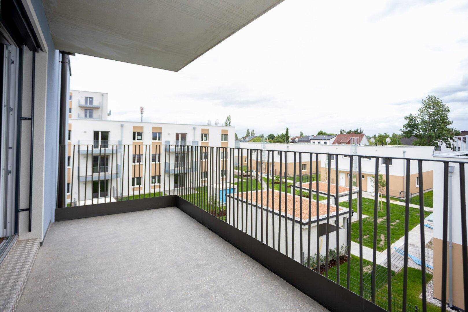 Balkon mit Metallgeländer und weitem Blick auf die Wohnanlage und Grünflächen.