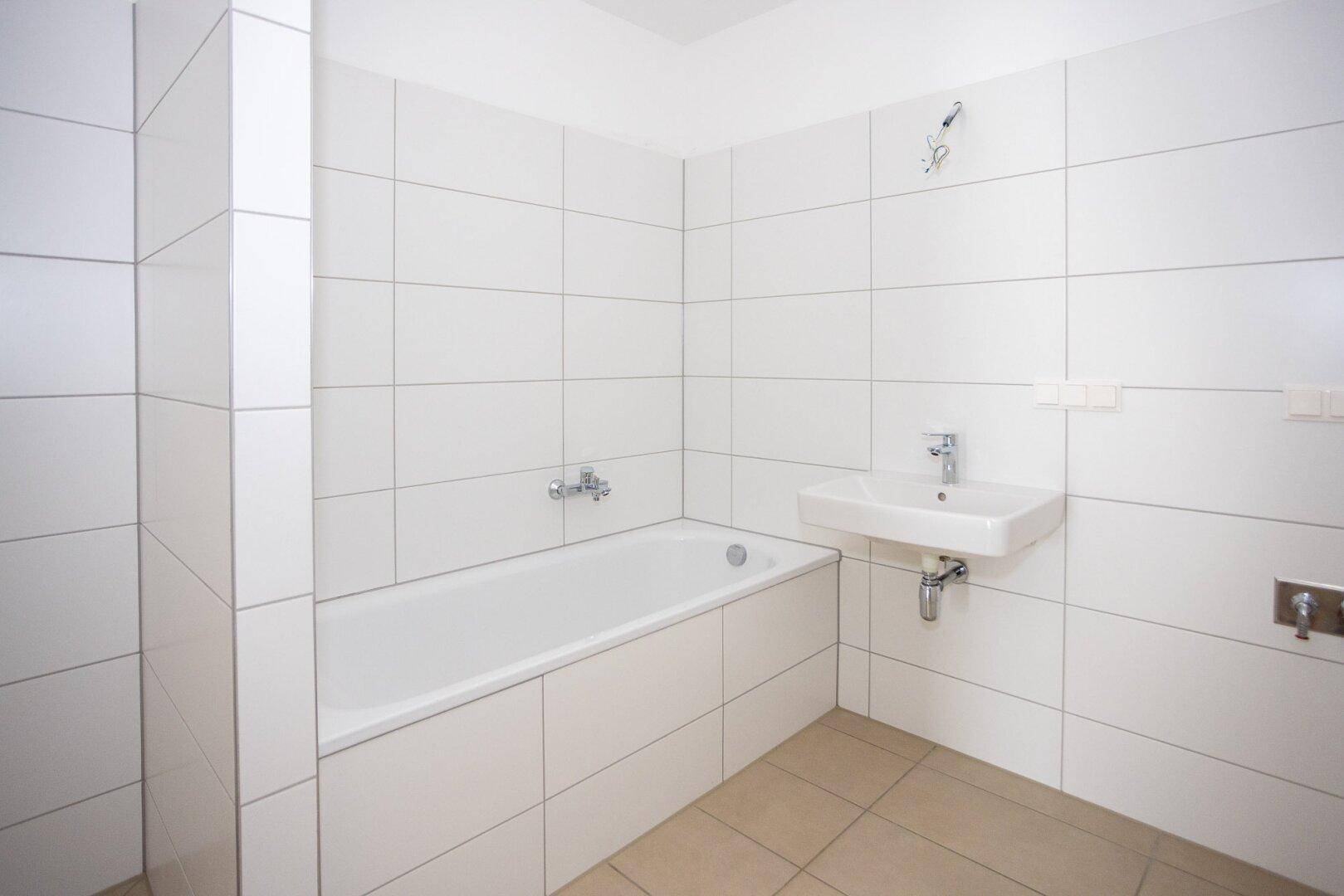Helles Badezimmer mit weißen Fliesen, Badewanne und Waschbecken.