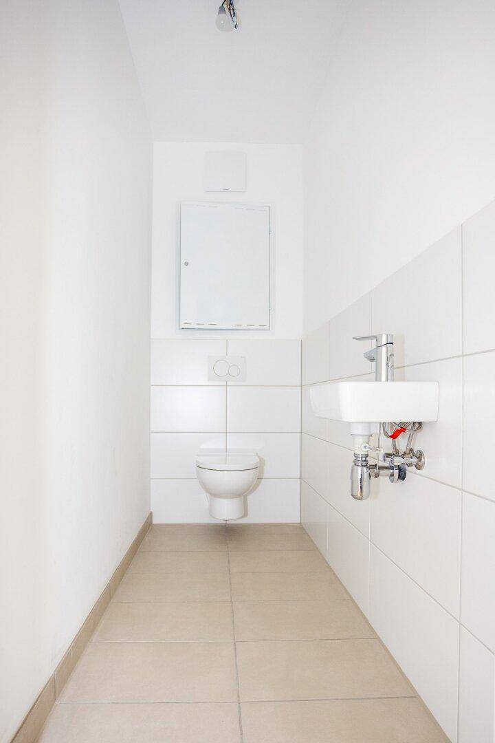 Schmale Gästetoilette mit wandhängendem WC und kleinem Waschbecken.