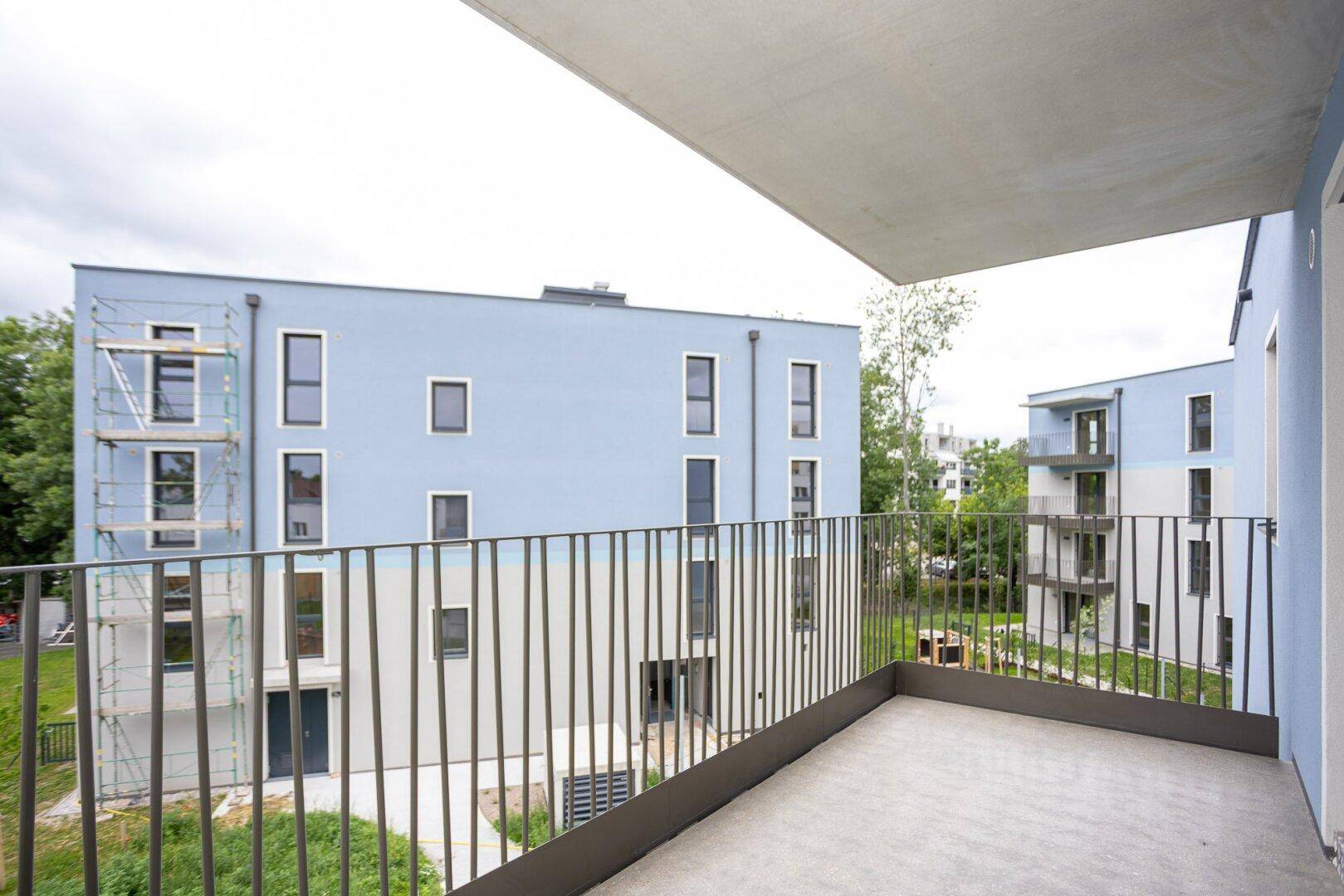 Balkon eines Neubaus mit Blick auf andere Gebäude und grüne Umgebung.