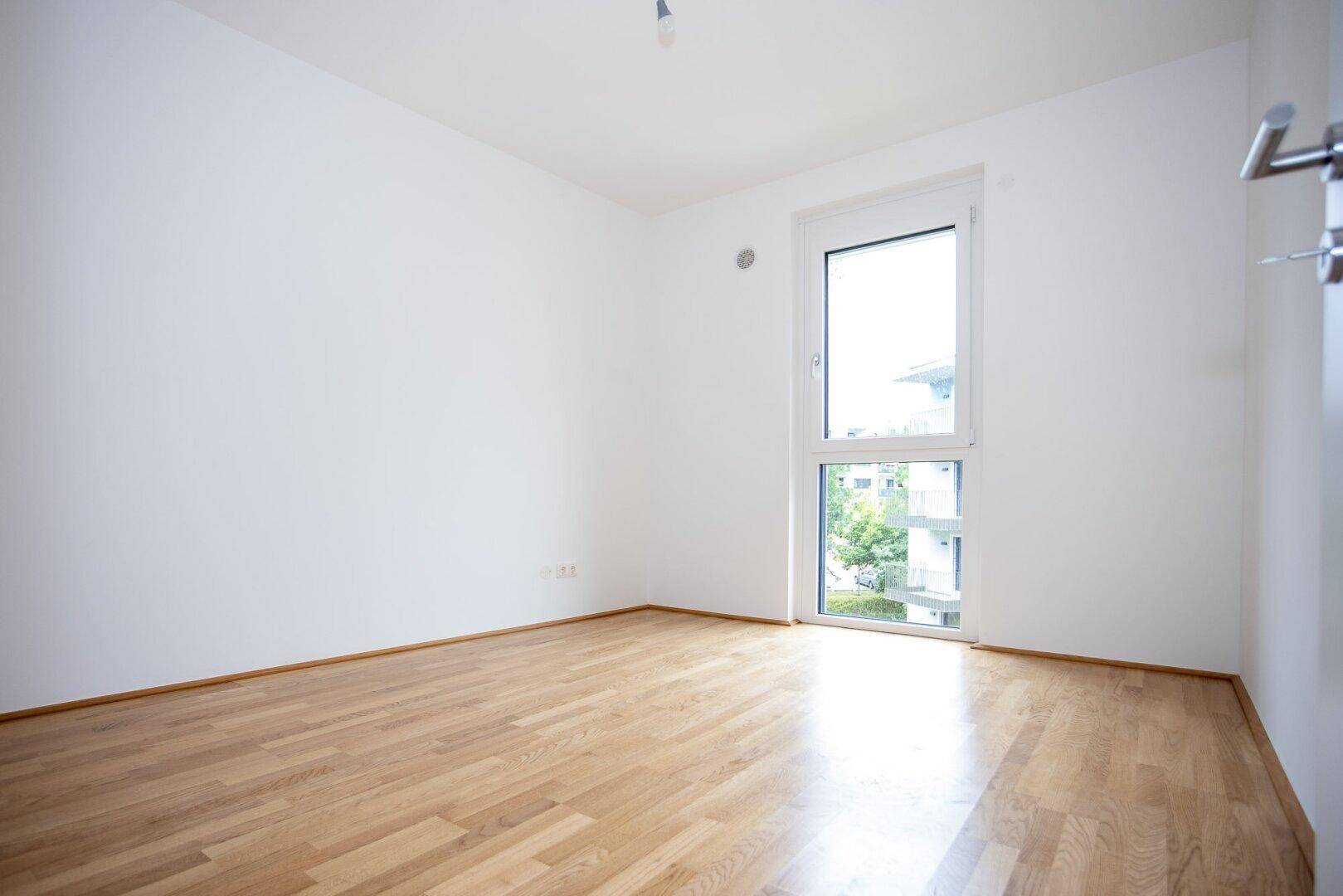 Helles Schlafzimmer mit Parkettboden und großem Fenster, bereit zur Einrichtung.