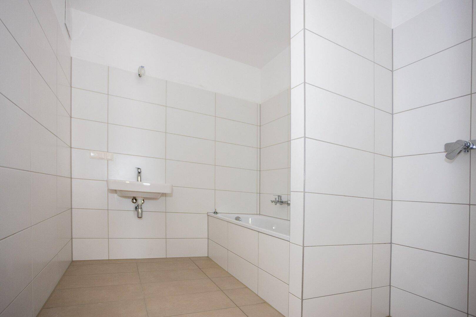 Modernes Badezimmer mit weißen Fliesen, Badewanne und Waschbecken.