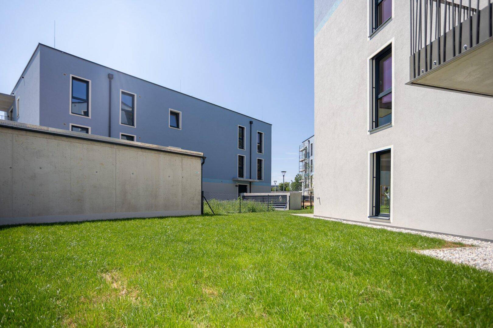 Außenbereich eines Wohnkomplexes mit Rasenflächen und modernen Gebäuden unter blauem Himmel.