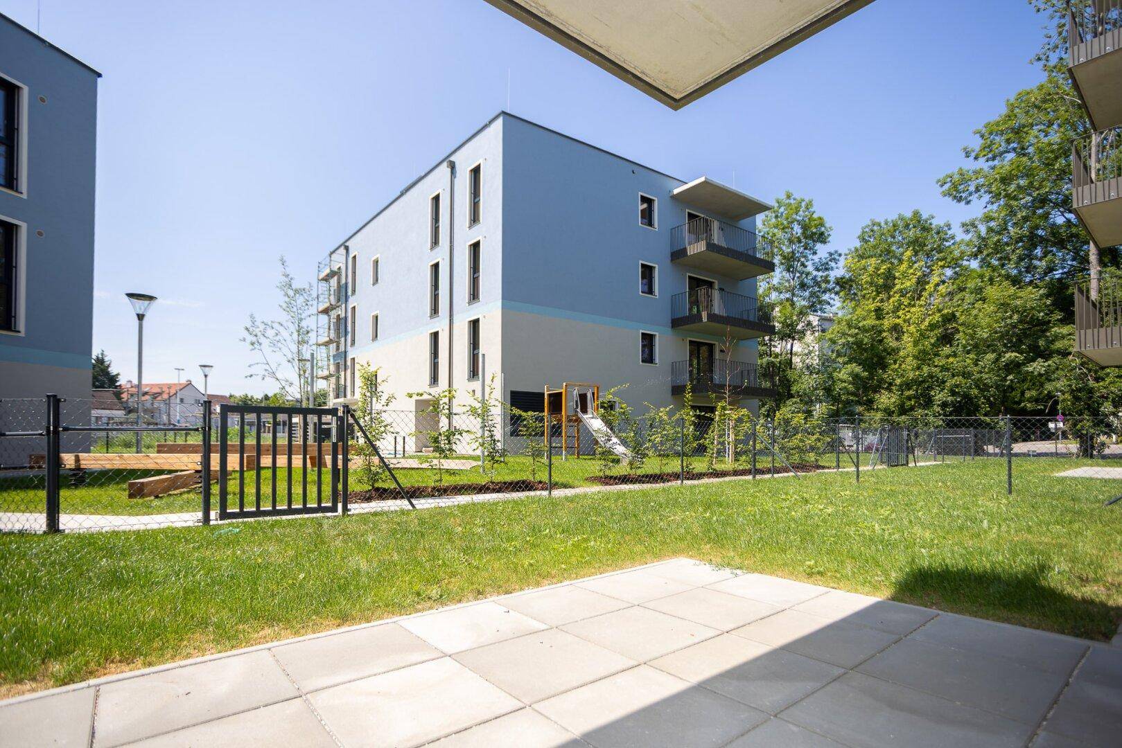 Außenansicht eines modernen Wohnkomplexes mit Spielplatz und gepflegten Grünflächen für Familien.