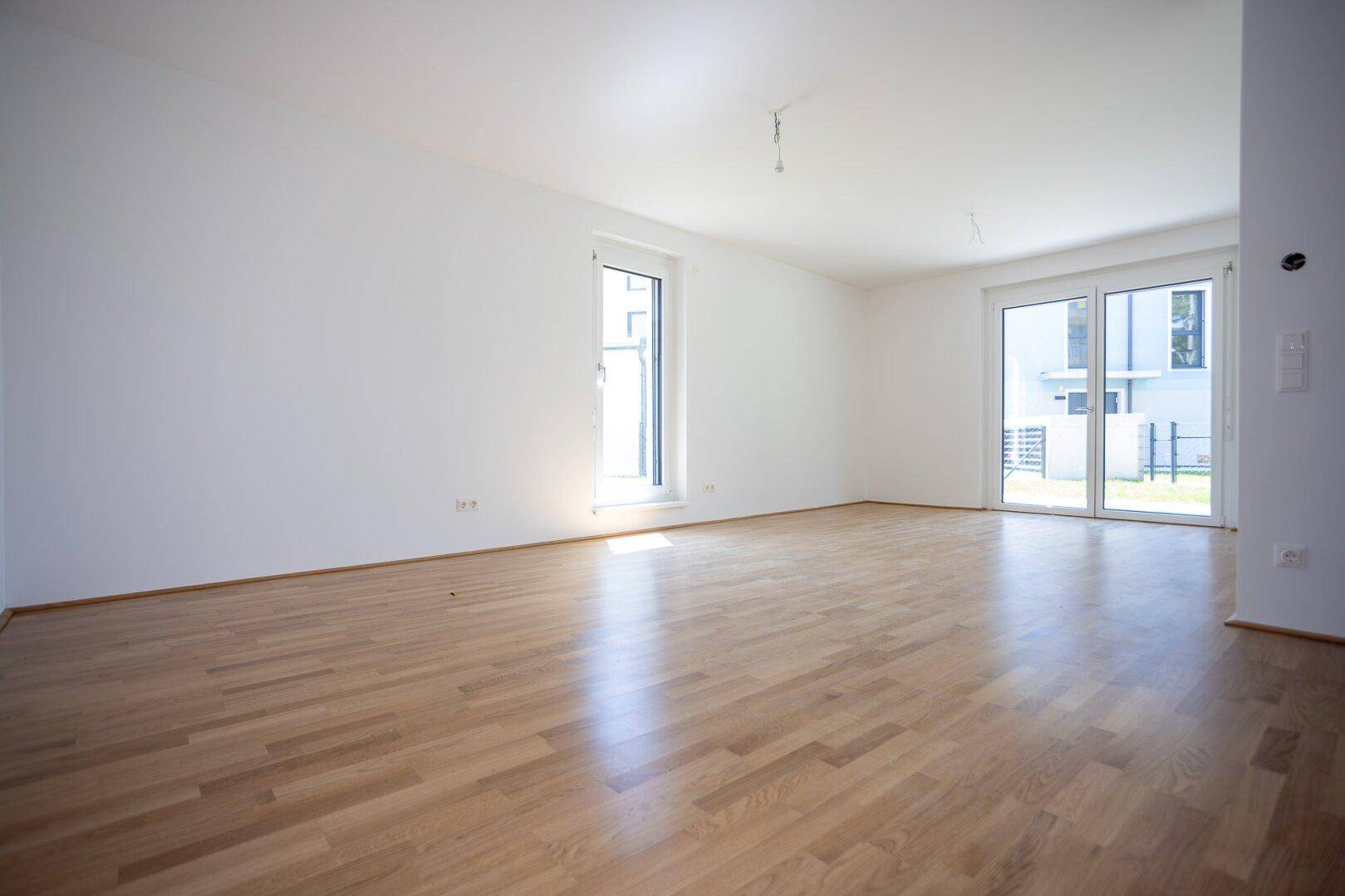 Helles, leeres Wohnzimmer mit Parkettboden und Zugang zum Garten, bereit zum Einzug.