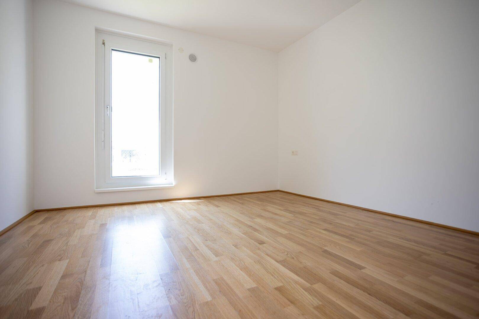 Helles Schlafzimmer mit großem Fenster und Parkettboden, ideal für Ruhe und Entspannung.